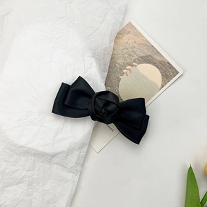 Detail of elegant black satin hair clip featuring a layered bow and central rose