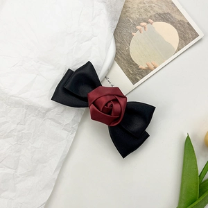 Close-up of elegant black satin bow hair clip with a deep red rose on a white background