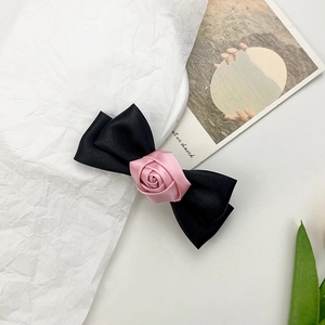 Detailed top view of an elegant black satin bow hair clip with a pink fabric rose center
