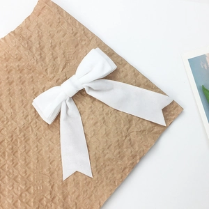 Close-up of white velvet bow hair clip with long ribbons on minimalist paper background