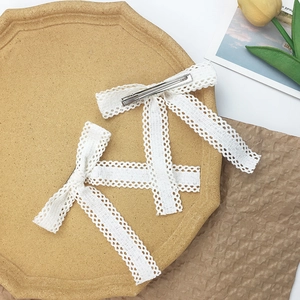 Elegant white lace bow hair clip with long ribbons and metal alligator clip on a tray