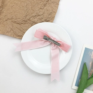 Pink velvet bow hair clip with long ribbons on a white ceramic plate background