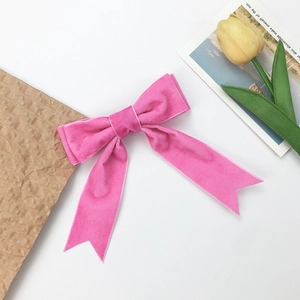Detail view of a pink velvet bow hair clip with long ribbons on a white background