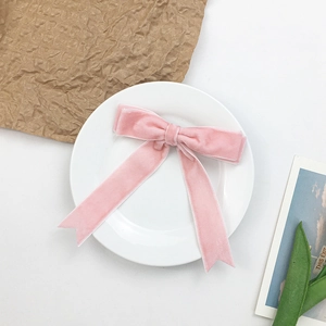 Close-up of a pink velvet bow hair clip with long ribbons on a white porcelain plate
