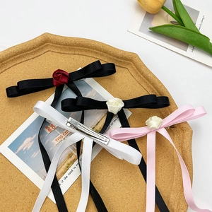 Elegant rose bow hair clips with long ribbons in black, white, and pink set on a tray