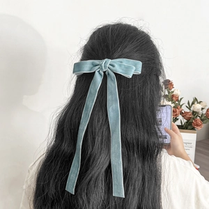 Detail view of a soft blue velvet bow hair clip with long ribbons on wavy hair