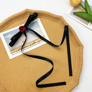 Detail of elegant black silk bow hair clip with red rose bud and long ribbon streamers