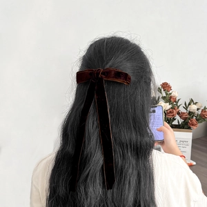Close-up of a burgundy velvet bow hair clip with long ribbons on dark hair