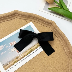 Detailed close-up of a black satin bow hair clip on a natural cork tray background