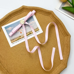 Pink ribbon bow hair clip with white fabric rose on a decorative cork tray