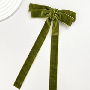 Close-up of dark green velvet bow hair clip with long ribbons on white background