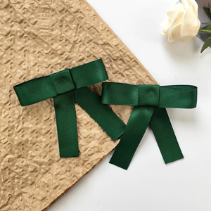 Dettaglio di fiocchi per capelli in raso verde scuro con nastri su sfondo floreale
