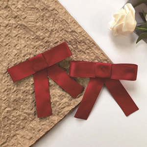 Dettaglio di due eleganti fermagli per capelli a fiocco in raso rosso vino satinato