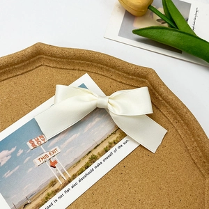 Detail view of a cream satin bow hair clip placed on a wooden tray with a tulip