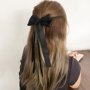 Detailed view of elegant black satin bow hair clip with long ribbons on a half-up hairstyle