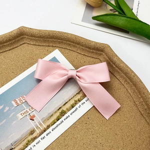 Pink satin bow hair clip with silky ribbon texture on a decorative aesthetic display tray