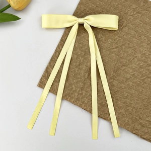 Détail d'une barrette nœud en satin jaune crème avec de longs rubans sur papier