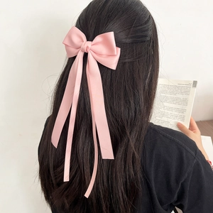 Pink satin bow hair clip with long ribbons shown on a model with long black hair