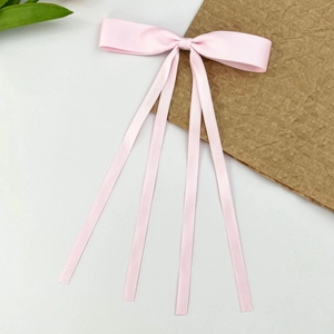 Gros plan d'une barrette à nœud en satin rose avec de longs rubans sur fond blanc épuré