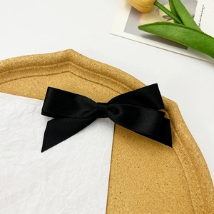 Detail view of black satin bow hair clip on a decorative tray with elegant silk texture