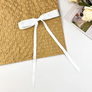 Elegant white satin bow hair clip with long ribbons on a minimalist decorative background