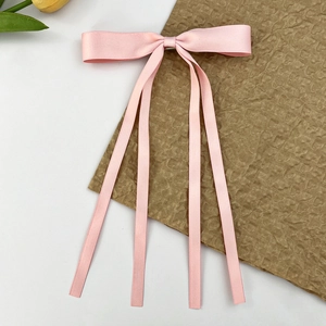 Détail de la barrette à nœud en satin rose avec de longs rubans et un éclat soyeux