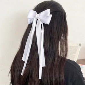 Detail of a large white satin bow hair clip with long ribbons on dark hair