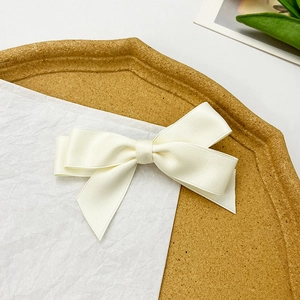 Detailed view of an off-white satin bow hair clip on a minimalist wooden tray