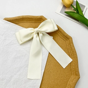 Elegant off-white satin bow hair clip with long ribbons on a decorative tray