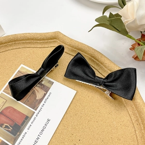 Detail of two black satin bow hair clips on a decorative tray with elegant prop card