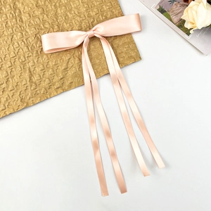 Detail of pink satin bow hair clip with long ribbons on white and gold background