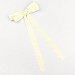 Detailed top view of a cream satin long tail bow hair clip on a minimalist white background