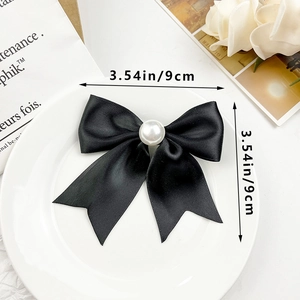 Détail d'un nœud en satin noir de 9 cm avec perle centrale sur une assiette blanche