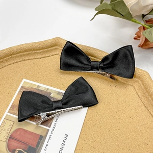 Pair of elegant black satin bow hair clips on a natural tray, classic minimalist hairpins
