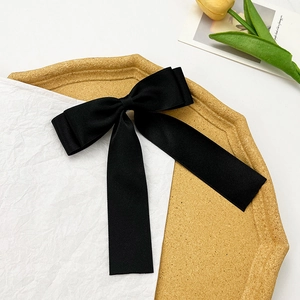 Elegant black satin bow hair clip with long ribbons on a yellow decorative tray
