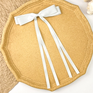 Elegant white satin double bow hair clip with long silk ribbons on a wooden tray