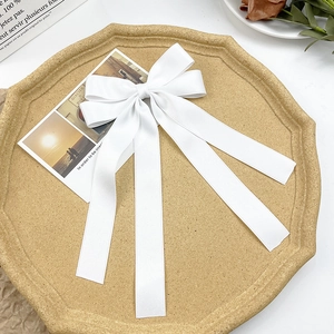 Detail of elegant white satin bow hair clip with long ribbons on a textured tray