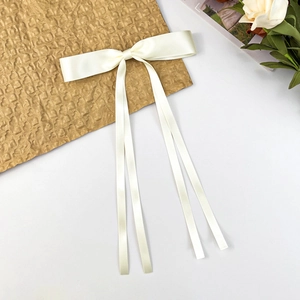 Close-up of elegant ivory satin bow hair clip with long ribbons on a textured paper