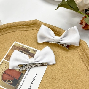 Close-up of dual white ribbon bow hair clips with silver metal alligator grip