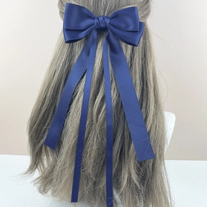 Detail of elegant navy blue satin bow hair clip with long ribbons on light brown hair