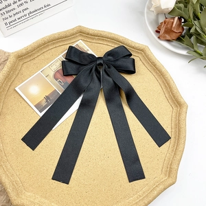 Detail showing elegant black satin bow hairclip with long ribbons on a vintage tray