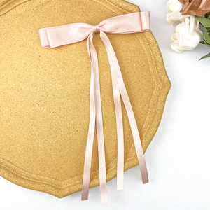 Detail of elegant champagne pink satin double bow hair clip with long ribbons on stone tray