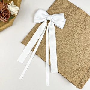 Detailed view of an elegant white satin bow hair clip with flowing long ribbons on paper