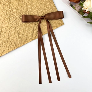 Detailed view of a brown satin bow hair clip with long ribbons on gold paper