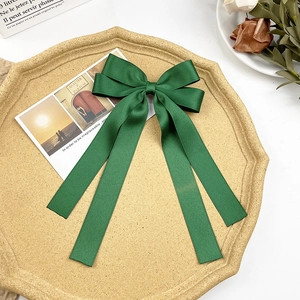 Detail of dark green satin bow hair clip with long ribbons on a decorative beige tray