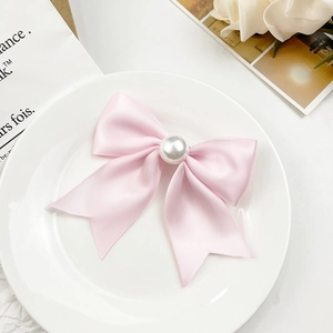 Barrette à cheveux avec nœud en satin rose et perle centrale sur une assiette décorative