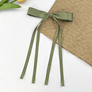 Gros plan sur une pince à cheveux en satin vert avocat avec des rubans sur fond épuré