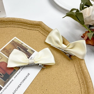 Pair of cream satin bow hair clips with silver alligator grips on cork tray