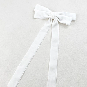 Elegant white velvet bow hair clip with long streamers on a neutral textured background