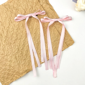 Détail de barrettes à nœuds en soie rose avec de longs rubans sur papier texturé